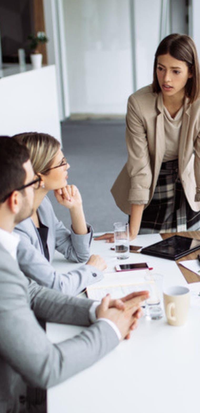 Eine Führungskraft spricht im Stehen mit ihrem Team am Besprechungstisch